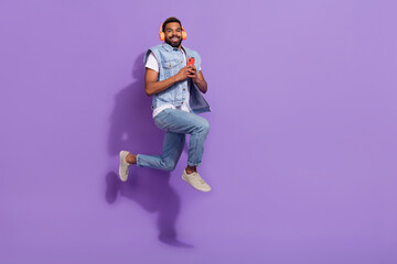 Full length photo of funky sweet guy dressed denim vest headphones jumping modern device empty...