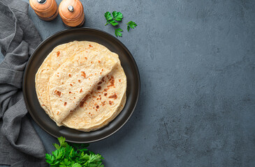 Traditional chapati tortillas with fresh parsley on a graphite background. Indian cuisine. Top...