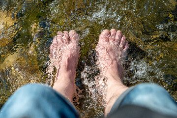 Flowing water between stones laps a man's feet in the sunshine