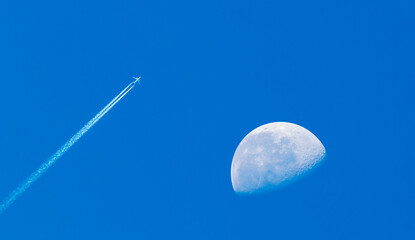 Clear blue sky with plane and half moon.