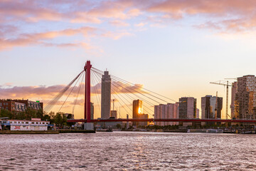 Obraz premium Bright sunset skyline of orange cable bridge and the Erasmus bridge and Euromast in the background with dramatic clouds