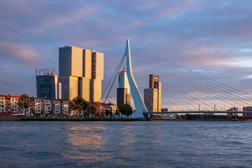 Fototapeta na wymiar Lit up skyline of Rotterdam with part of the famous Erasmus bridge in the foreground and architecture of typical modern skyscrapers at sunset