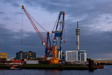 Industrial inland shipping colourful cranes in port at sunset blue hour. Engineering heavy machinery architecture and logistics concept	