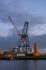 Fototapeta na wymiar Vertical frame of industrial inland shipping colourful cranes in port at sunset blue hour. Engineering heavy machinery architecture and logistics concept