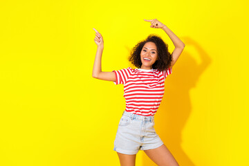 Naklejka premium Portrait of young attractive happy woman directing empty space summer clothes shop isolated on yellow color background