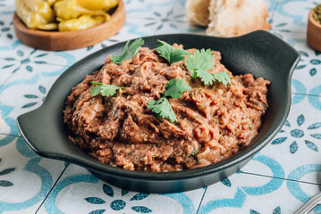 Mashed red bean with spices on blue tiles background. Traditional georgian dish lobio in black plate with bread and pickled hot peppers.