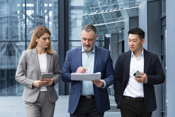 Diverse business team three colleagues employees discuss documents contract outside office building...