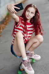 Girl teenager with red hat,with skateboard and smartphone, taking selfie outdoors