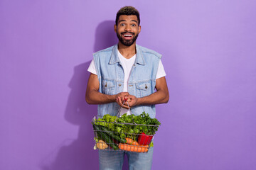 Photo of pretty impressed guy dressed denim vest holding green veggies basket empty space isolated purple color background