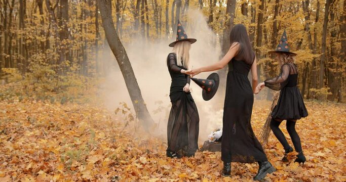 Three women in halloween costumes dnce around cauldron