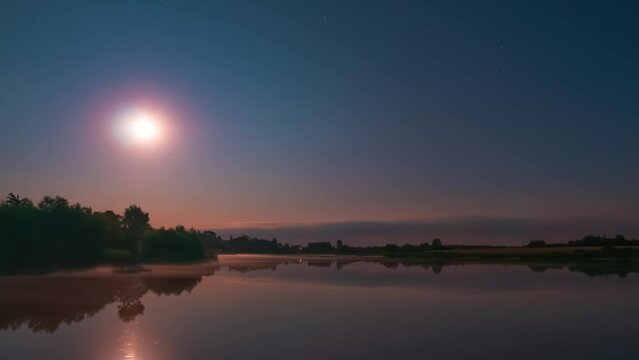 Starry night on a calm lake with flat water surface. Stars and moon timelapse