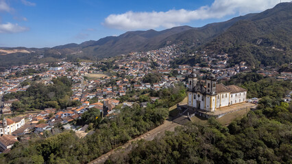 Visão panoramica de igreja em cidade histórica de Ouro Preto Minas Gerais em meio a montanhas e céu nublado construções e casas antigas ao fundo