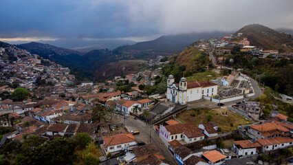 Visão panoramica de igreja em cidade histórica de Ouro Preto Minas Gerais em meio a montanhas e céu nublado construções e casas antigas ao fundo