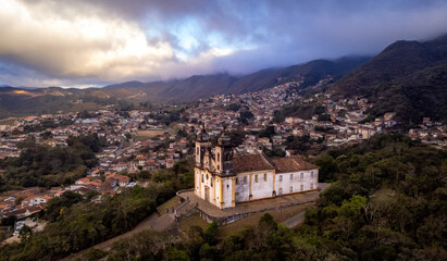 Fototapeta na wymiar Visão panoramica de igreja em cidade histórica de Ouro Preto Minas Gerais em meio a montanhas e céu nublado construções e casas antigas ao fundo