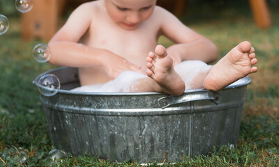 A little boy bathes, washes in an iron basin. A happy child splashes in the water. Vintage. The...