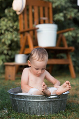 A little boy bathes, washes in an iron basin. A happy child splashes in the water. Vintage. The concept of child hygiene. Soap bubbles, a bubble bath.