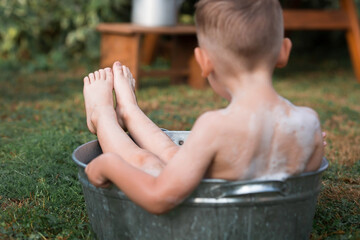 A little boy bathes, washes in an iron basin. A happy child splashes in the water. Vintage. The concept of child hygiene. Soap bubbles, a bubble bath.