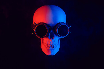 human skull in steampunk glasses with red and blue neon light on a black background