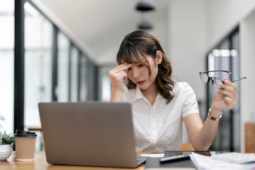 Depressed businesswoman. Young beautiful asian business woman suffering stress working on laptop at office.