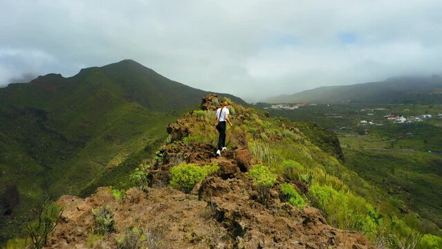 Attractive woman walking in dangerous mountain. Pretty girl runs along path on cliff. Cactus bushes, rocky volcanic landscape. Aerial. Athlete, hill ridge. Tamaimo. Way, Risco Blanco. Tenerife.