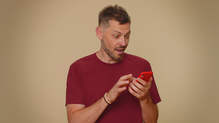 Happy excited joyful young man use smartphone typing browsing say wow yes, found out great big win news doing winner gesture. Adult stylish male guy isolated on beige studio wall background indoors