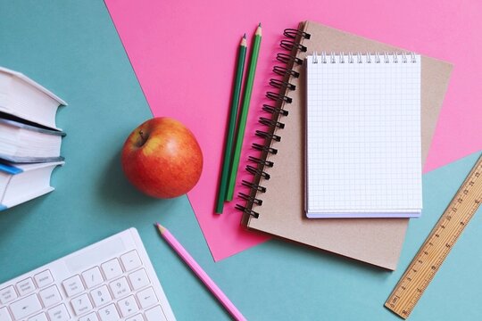 Back to school concept flat lay photo. Books, computer keyboard, notepad, pencils, wooden ruler, apple on a table