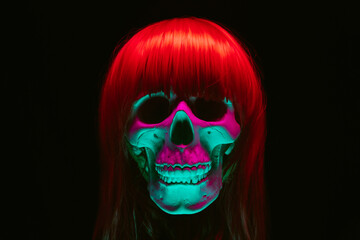 human skull of a woman in a wig with red hair with colored pink green light on a black background