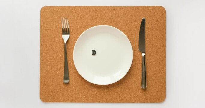 The text DIET appears on the plate. Plate, fork and knife on a cork napkin. 4K stop motion animation