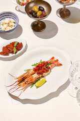Seafood appetizer - baked langoustines with tomato tartar on white table. Grilled shrimp in italian restaurant menu. Langoustines on white background with shadows. Shrimp appetizer. Baked prawn.