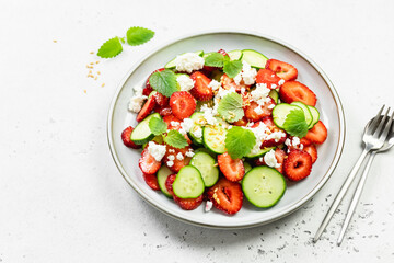 Healthy cucumber strawberry feta cheese salad with lemon dressing on plate. Top view, flat lay, copy space.
