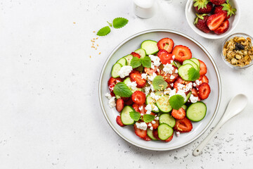 Healthy cucumber strawberry feta cheese salad with honey lemon dressing on plate. Top view, flat lay, copy space.