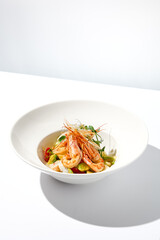 Elegant food - salad with shrimp and avocado on white table with harsh shadow. Flashy food concept. Seafood salad with shrimp, tomatoes and avocado on white plate with sunlight.