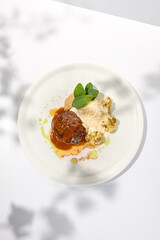 Beef cutlet with grilled cauliflower with gravy and cheese sauce on white plate. Elegant beefsteak on light background with shadows of sunlight. Summer menu hard shadows Meat ball of minced meat