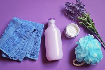 Wellness and spa cosmetics for hair and skin care. Blue towel, purple shampoo bottle, moisturizing cream, sponge and lavender flowers. Flat lay beauty photography