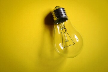 Electric light bulb on yellow background photo top view. Electricity consumption