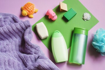 Baby care cosmetics, natural bath products. Purple towel, green shampoo bottle, shower gel, soap bar, sponge and rubber toys flat lay photo