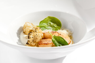 Gourmet dish - pan seared sea scallops with mashed potatoes, grilled cauliflowers on white plate. Scallops with vegetables and creamy espuma. Delicacy seafood in restaurant menu.