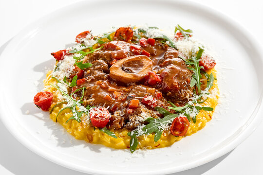 Traditional Italian dish - osso buco with risotto Milanese and cherry tomato and rucola. Ossobuco with saffron rice isolated on white background. Stewed meat on bone with yellow risotto.
