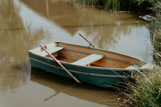 Wooden green boat with oars at the shore of a lake or pond in summer