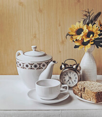 Tea time and whole wheat bread. Enjoy and refresh your morning with a cup of hot tea. Delicious breakfast and healthy aromatic beverage. Cup with teapot and flowers in a vase.