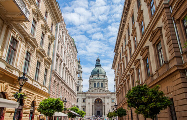 Fototapeta na wymiar Old town street buildings and the St. Stephen's Basilica, a Roman Catholic Cathedral in the old town of Budapest, Hungary, Europe. Church tower among historical houses. Urban downtown neighborhood.