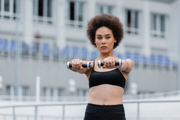 young african american sportswoman looking at camera while exercising with dumbbells.