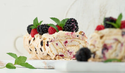 Baked meringue roll with cream and fresh fruits on a white wooden board, delicious dessert