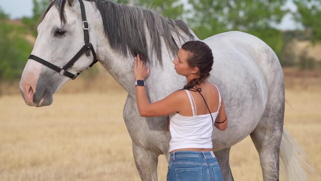 Side view of a young woman petting and taking care of her white horse