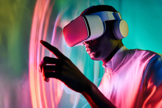 Serious black man touching large screen while exploring virtual reality in modern headset