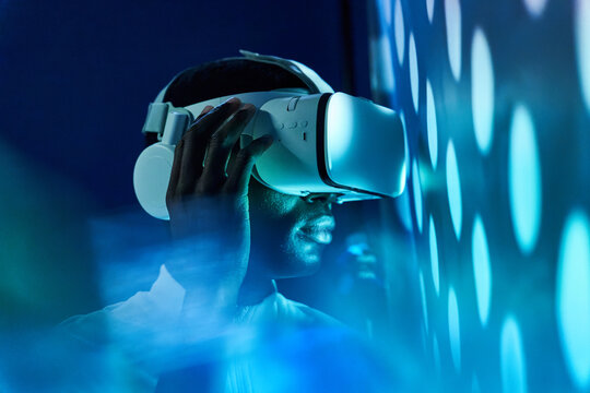 Black man touching large screen while exploring virtual reality in modern headset