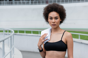 young african american woman in fitness tracker standing with white towel on shoulder.