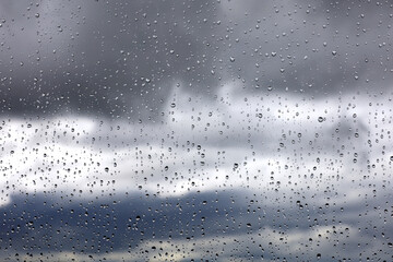 Raindrops on window glass on blurred background of sky with storm clouds. Beautiful water drops, rainy weather