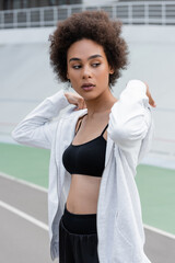 Fototapeta na wymiar sportive african american woman in black sports bra and white sports jacket looking away.