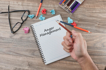 A notebook with Anger Management text and cropped hand breaking a pencil on a wooden office table